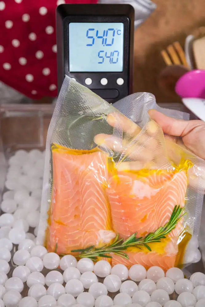 Das Foto zeigt die Hand einer Person die einen Vakuumbeutel mit verpacktem Fischfilet vor ein Thermometer hält.