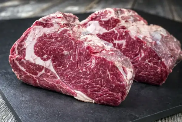 Das Bild zeigt 2 dicke marmorierte Stücke rohes Fleisch auf einer schwarzen Unterlage.