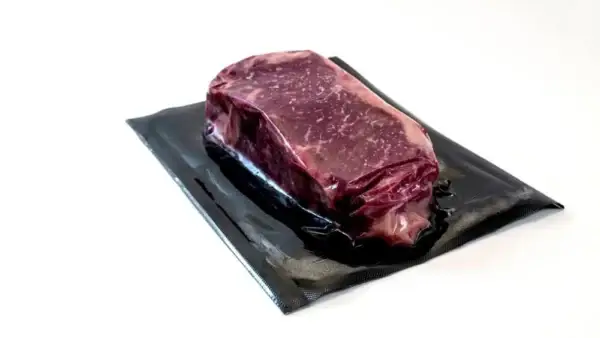 Das Bild zeigt ein Stück rohes Fleisch in einen schwarzen Vakuumbeutel einvakuumiert.