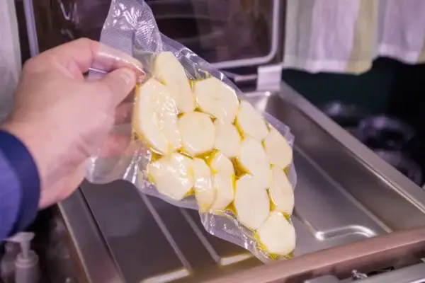 Auf dem Bild sieht man die Hand einer Person die einvakuumierte Kartoffeln aus einen Vakuumgerät nimmt.