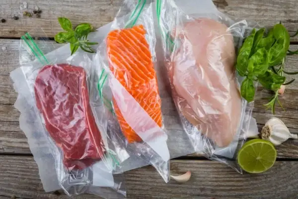 Auf dem Bild sieht man verschiedene Fleisch und Fischsorten in Vakuumbeuteln auf einer Holzoberfläche liegend.