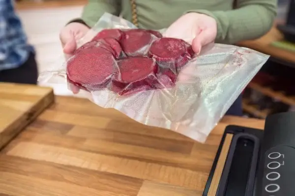 Ein strukturierter Vakuumbeutel mit einigen vakuumierten rote Beete Scheiben in den Händen einer Frau.